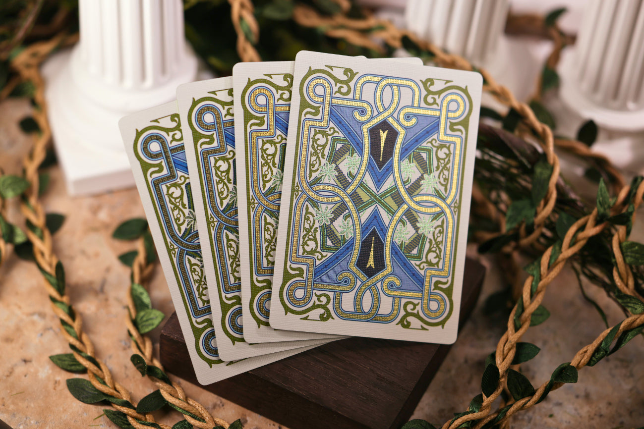 Four Signature Edition card backs with decorative designs on a wooden surface with greenery.