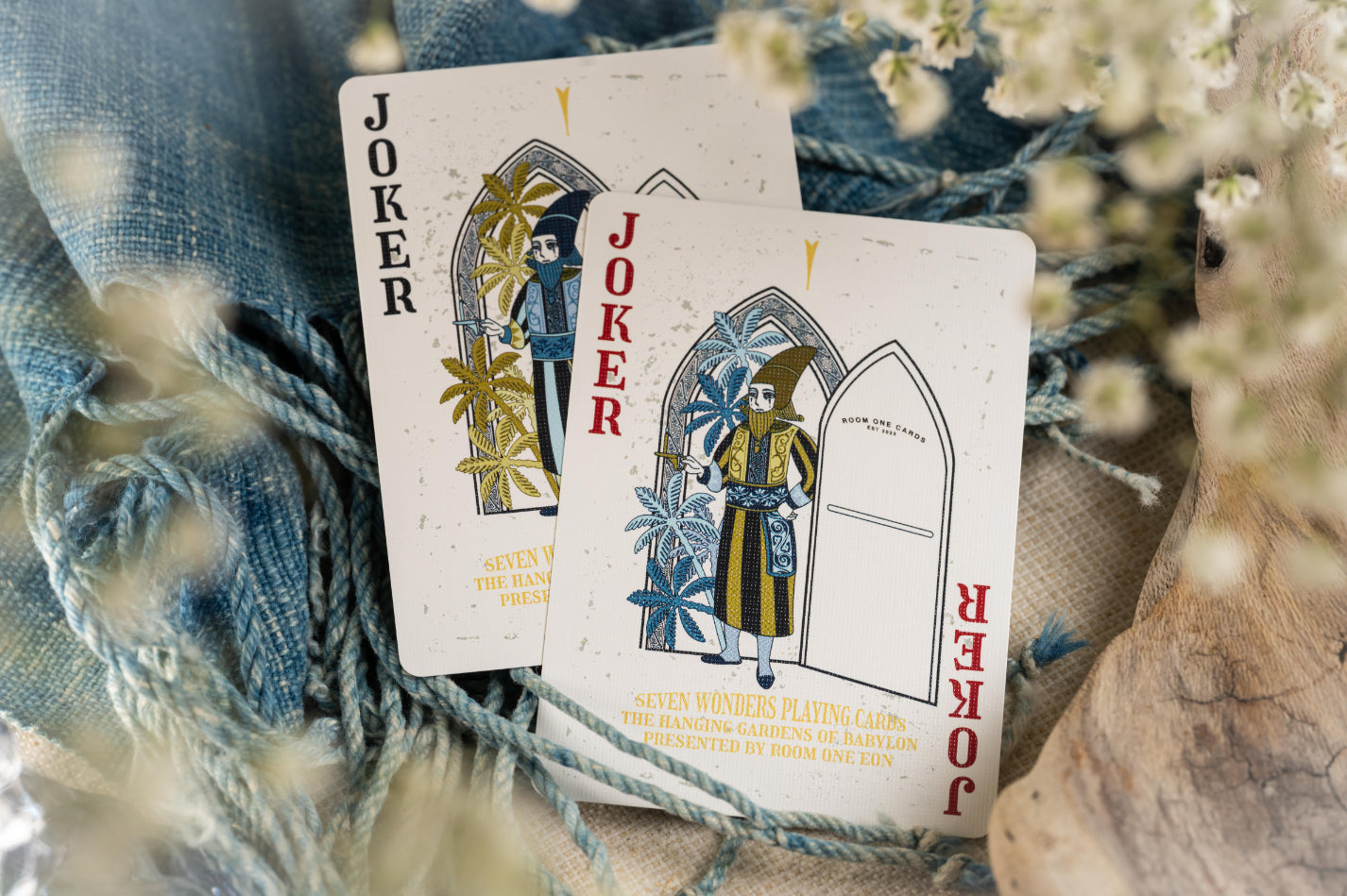 Two joker cards from a deck with decorative design on a textured surface with flowers.