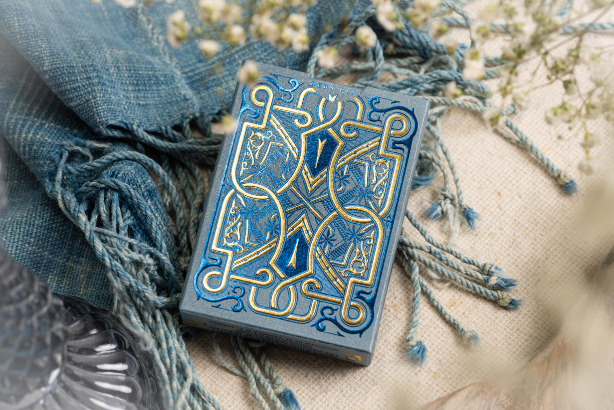 Decorative tuck box with intricate blue and gold design on a textured surface with fabric and flowers.