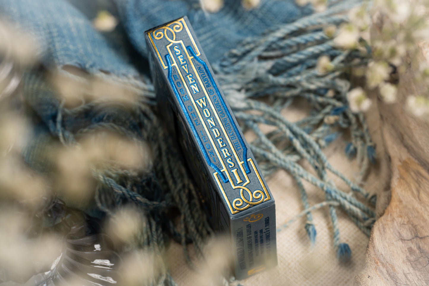 Blue and gold box with decorative text on a textured surface with blurred flowers in the background