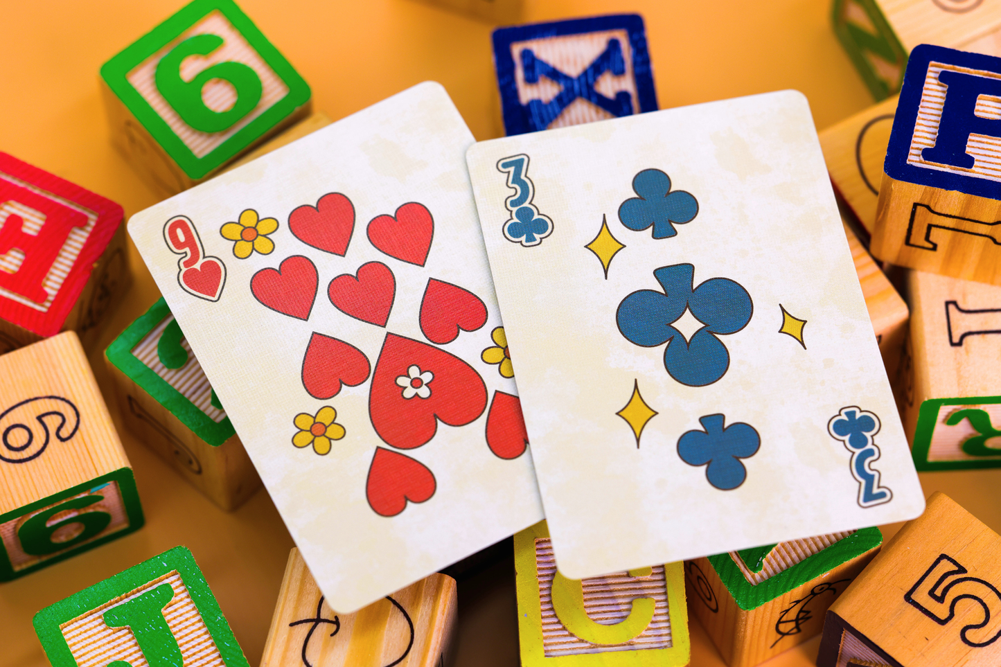 Two playing cards (hearts and clubs) on a background of colorful wooden blocks with numbers and letters.