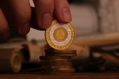 A collector's coin with the Assassin's Creed logo on it, placed on a stack of similar coins.