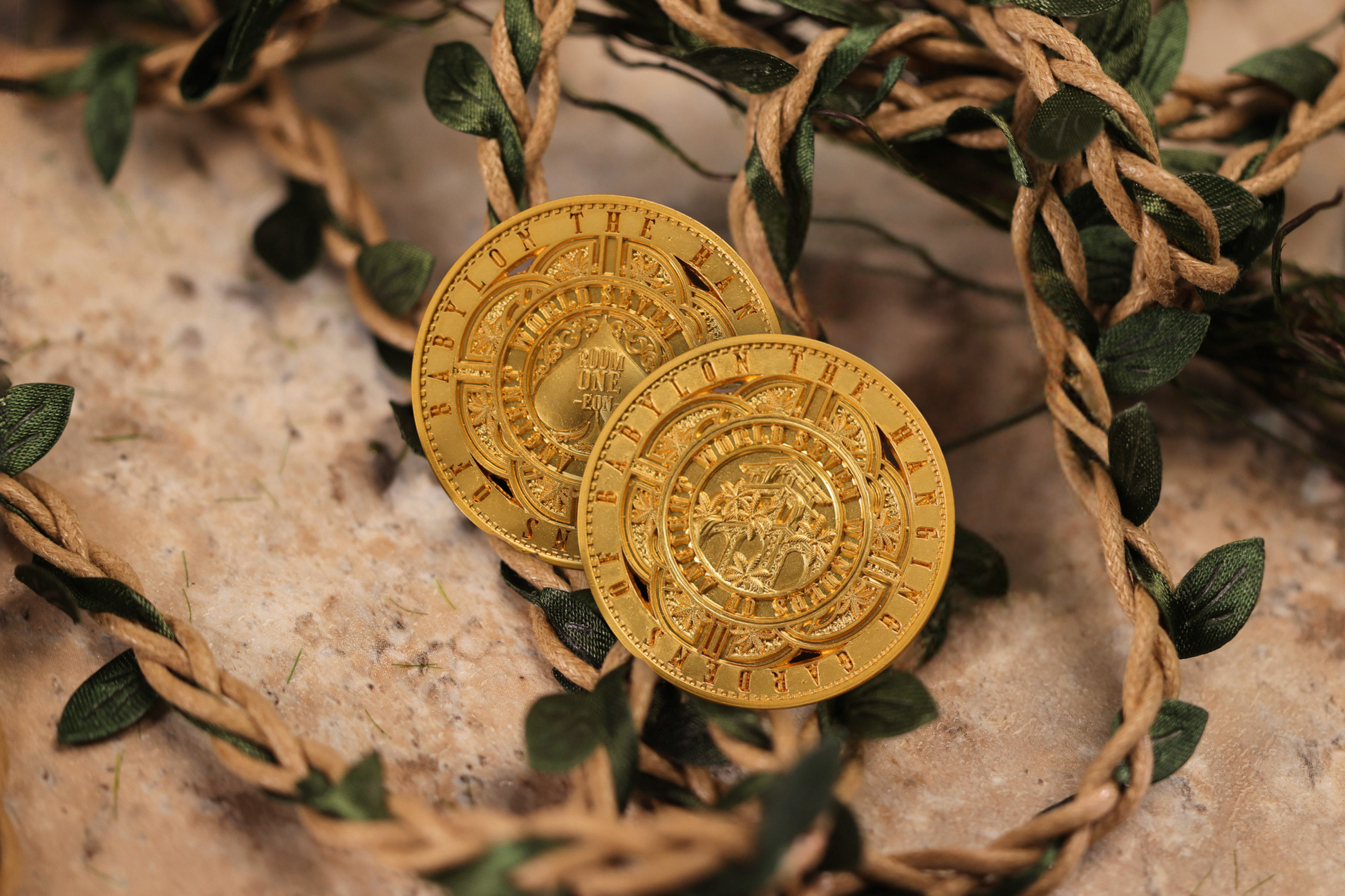Two gold coins with intricate designs on a stone surface with greenery
