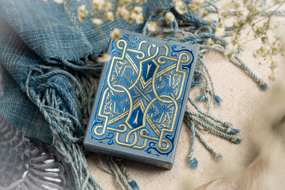 Decorative tuck box with intricate blue and gold design on a textured surface with fabric and flowers.