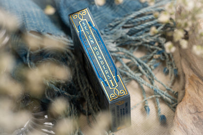 Blue and gold box with decorative text on a textured surface with blurred flowers in the background