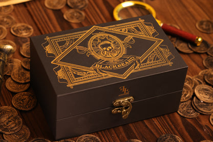 Black collector's box with gold detailing on a wooden surface with coins and a magnifying glass.