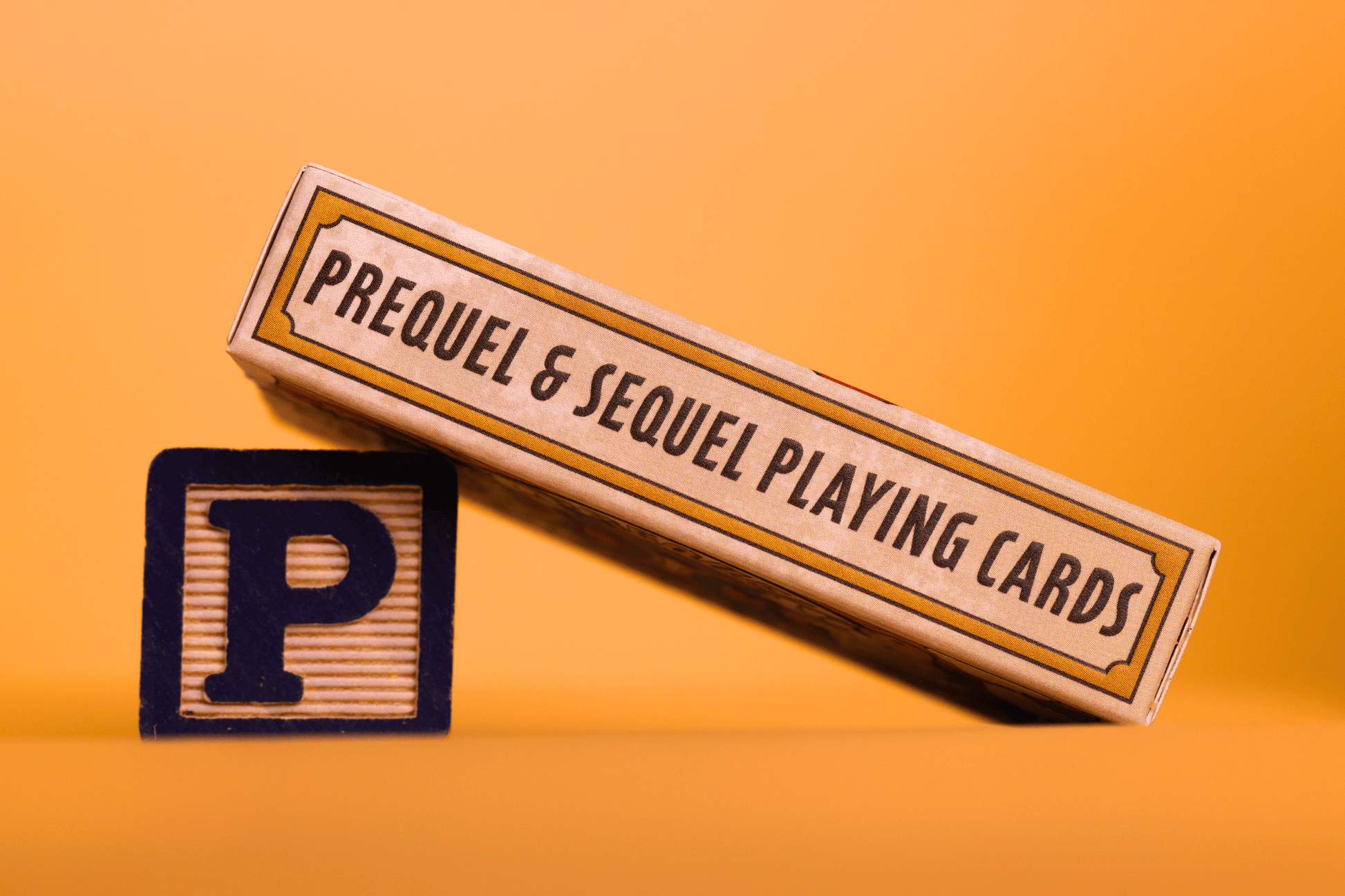 Side view of the 'Prequel Playing Cards' with a wooden block letter 'P' on an orange background