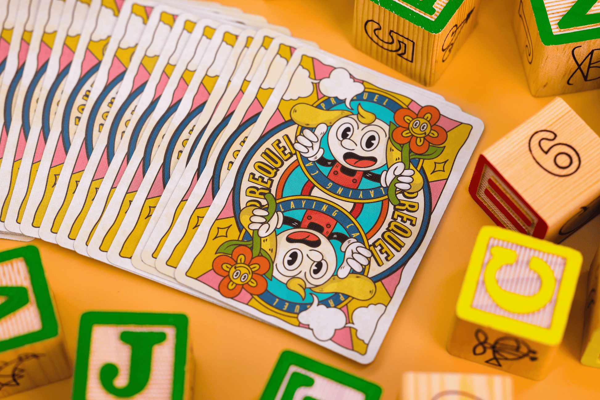 Prequel Edition Card Backs feature colorful playing cards with cartoon characters on a yellow surface with wooden blocks.