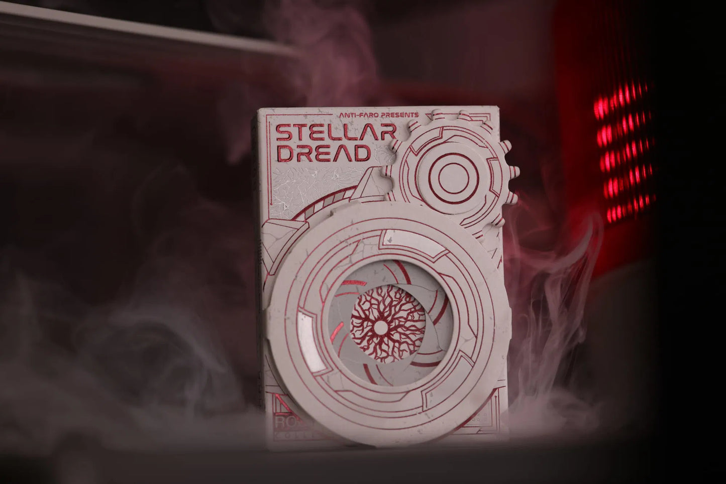 A close-up of the Stellar Dread playing cards tuckbox, featuring intricate, geometric designs with a hatch door mechanism, with a red light in the background.