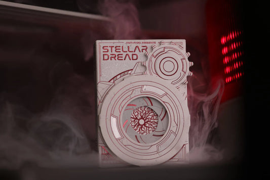 A close-up of the Stellar Dread playing cards tuckbox, featuring intricate, geometric designs with a hatch door mechanism, with a red light in the background.
